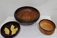 Three wooden bowls grouped on white surface: a large natural wood grain bowl, a shiny bowl with dark rim stripe, and an Asian-style bowl with yellow leaf decorations inside.