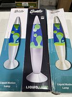 Three Jambo lava lamps in original packaging, showing front views and box design including blue liquid and yellow wax inside, silver base and cap.