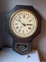 Front view of antique New Haven wall clock showing octagonal wooden frame and clock face with Roman numerals and calendar dates.