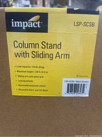 Close-up of product label on box showing brand Impact, model LSP-SCSB, and features like load capacity, max height, sliding arm with pistol grip, locking wheels, removable extension column, reversible pin sizes.