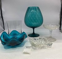 Front view showing all five glass items arranged together: blue wavy bowl, tall clear vase, large blue stemmed goblet, clear pedestal bowl, and clear square ashtray/small bowl.