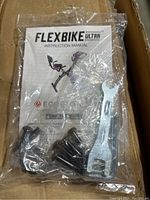 Plastic bag containing Flexbike Ultra instruction manual, multiple black bolts, and a double-ended metal wrench tool.