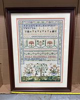 Full front view of the framed needlepoint sampler showing its entire design, colors, and frame.