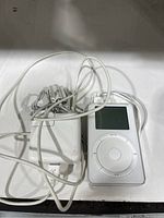 Apple iPod Classic with charger and earphones tangled together, showing the device and accessories from a side view.