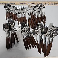 Top down overview showing the full large lot of Ekco Mid-Century Modern flatware spread out including forks, knives, spoons and serving utensils with distinctive brown wooden handles and patterned stainless steel ends.