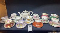 Full set display of 12 floral teacups and saucers with Sadler tea kettle on left side