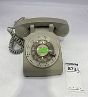 Front view of the sage green rotary phone showing rotary dial, handset resting on base, and coiled cord.