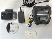 Overview photo of the lot showing two Zebra QLn420 mobile printers, a Zebra handheld device, power adapter, and software CD.