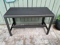 Front view showing rectangular resin wicker console table against fence