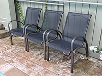 Three black mesh seating outdoor armchairs with aluminum frames, arranged side by side on stone patio, showing minor scratches and one chair with sap residue.