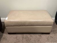 Front view of a cream leather ottoman showing overall shape and condition.