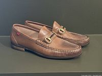 Side angle of the pair of brown leather Marc Joseph loafers showing metal bit detail and wear signs on heel and upper leather.