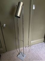 Full view of floor lamp showing square base, dual pole support, cylindrical shade.