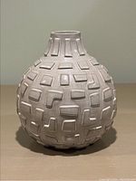 Front view of round ceramic vase with geometric raised rectangular pattern, light beige color.