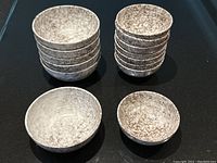 Overview photo showing stacks of larger and smaller bowls with speckled pattern on black surface.