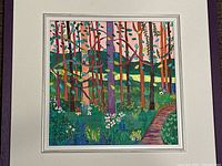 Framed colorful abstract forest scene painting showing a variety of multicolored trees, flowers, and a path in a green and pink landscape.