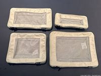 Set of four tan Monos travel storage kits arranged on dark surface showing various sizes, mesh tops, and zipper edges.