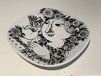 Top view of square porcelain art dish showing the detailed floral and face design in black on white background.