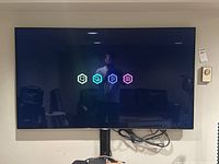 Samsung 60" TV powered on displaying startup icons, mounted on wall, cables visible