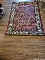 Full view of the rug laid on a wood floor showing the detailed Persian style floral pattern and red and cream colors.