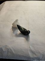 Two small animal sculptures on white cloth background, a dark green polished soapstone bird and a white matte alabaster polar bear