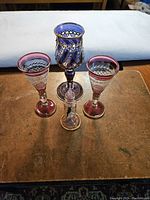 Four mouth blown glass pieces including a large blue wine glass with gold bands, two smaller pink liquor glasses, and one small clear perfumerie bottle.