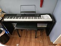 Front view of Casio RockJam keyboard on stand with bench underneath and manuals on the right side of the keyboard.