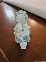 Front view showing two cherubs embracing on the front of the white porcelain shoe with green trim.