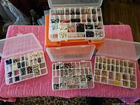 Overhead view of four plastic organizer boxes with assorted beads sorted in compartments on a pink towel-covered surface.