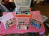 Four plastic bead organizer boxes on a pink towel, filled with assorted glass beads sorted by type and color