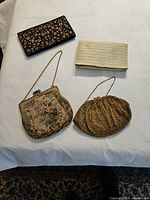 All four evening bags laid out on a white cloth background; black embroidered clutch, gold striped clutch, floral tapestry bag and gold beaded bag.