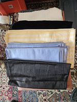 Various folded fabric pieces arranged on a floor with yellow striped, light blue solid, black velvet, and black mesh fabrics visible.