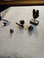 Overview of five bird figurines on a white cloth surface including a rooster on stand, flying bird, perched bird, and two smaller birds.