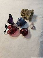 Photo showing four heart-shaped glass pieces and two mineral specimens on a neutral surface.