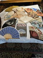 Full set of 11 hand fans arranged on white cloth with fan history book included