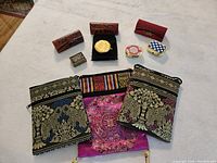 Overview of all items on white surface: 3 embroidered shoulder bags, 4 pill boxes, and 3 lipstick cases