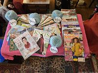 Overview photo showing all magazines spread out on a pink cloth along with four skeins of yarn.