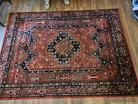Photo showing full view of Persian style area rug laid on wooden floor, highlighting the central medallion and colors.