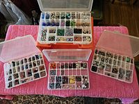 Top view of three plastic compartment organizers filled with assorted glass and metal beads in various colors and designs on a pink towel.