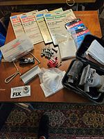 Full lot overview showing sander in case, sanding sheets, mini clamp, screws and sanding sponges on wooden surface.