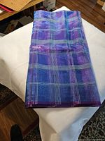 Folded piece of organza fabric in a purple and blue plaid pattern, showing fabric texture and color.