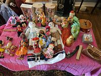 Wide view of toys on pink cloth including dolls, stuffed animals, and musical toys.