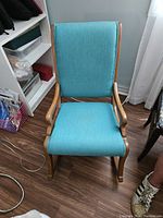 Front view of the oak rocking chair showing the blue upholstered seat and back with wooden curved armrests and rockers on a wood floor.