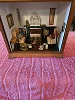 Front view of diorama shadow box with miniature furnishings including armchairs, piano, drum, birdcage, and accessories.