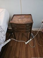 Front view of single bedside table showing worn top surface and three drawers with metal handles.