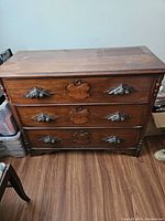 Front view of dresser showing three drawers with carved wooden plaques and metal leaf handles
