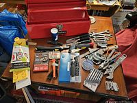 Overview photo showing red Husky toolbox and various hand tools on table including wrenches, chisels, screwdrivers, drill bits, socket set and level