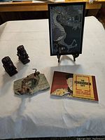 Wide view of all items in the lot including framed dragon artwork, lion statues, dragon figurine on stone base, and cultural booklet