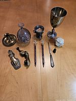 Full collection display of brass door knockers, glass dip pens, inkwell, goblet, candle holder, letter opener, and marble object on wooden table