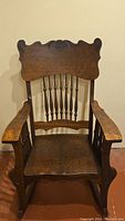 Front view of antique tiger oak rocking chair showing carved crest back and spindle design.